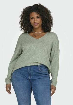Pull en v vert clair avec des poignets côtelés, présentant une coupe décontractée et une texture douce, associé à un jean bleu.
