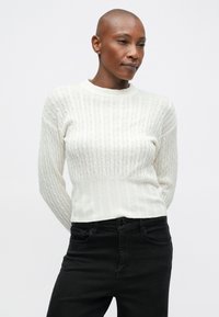 Suéter branco de malha com um padrão de nervuras texturizado, gola redonda e mangas longas, combinado com jeans pretos.
