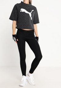 Czarna krótka bluza z białym logo Puma, krótkie rękawy, w połączeniu z czarnymi legginsami i białymi butami sportowymi. Teksturowany materiał o dopasowanym kroju.