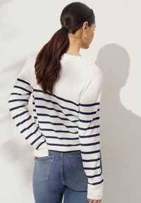 Wit en marineblauw gestreepte trui met lange mouwen, voorzien van een ronde halslijn en geribbelde manchetten; gedragen met blauwe spijkerbroeken.