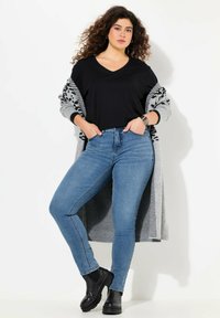 Camiseta negra de cuello en V, cárdigan gris con patrón, jeans ajustados azules y botas negras de tobillo, mostrando un ajuste relajado y texturas suaves.