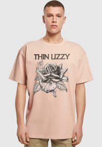 Šviesiai rožinė per didelė marškinė su trumpomis rankovėmis, kuriuose pavaizduota juoda grafiška rožė ir užrašas "THIN LIZZY" viršuje. Atsipalaidavęs siluetas ir apvalus iškirpimas.