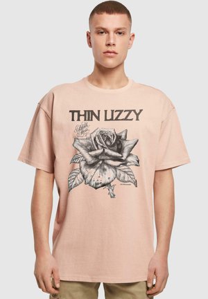 Lyserød oversized t-shirt med korte ærmer har et sort grafisk rosebillede og teksten "THIN LIZZY" ovenfor. Afslappet pasform og rund halsudskæring.