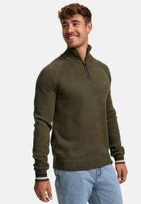 Olivengroen gebreide pullover met een kwart-rits kraag, geribbelde manchetten en streepaccenten op de manchetten en onderrand. Beschikt over een gestructureerd gebreid patroon.