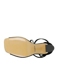 Sandal alta nera con tacco, dotata di una suola beige liscia, presenta sottili cinturini e un rinforzo posteriore. Logo del brand in rilievo discreto.