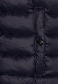 Navy puffer jacket featuring a quilted design, smooth texture, and a round black button closure at the front for secure fastening.