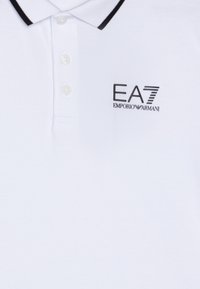 Weißes Poloshirt mit schwarzem Kragen und Logo. Verfügt über drei Knöpfe am Hals, aus strukturiertem Stoff gefertigt. Das Logo beinhaltet "EA7 EMPORIO ARMANI."