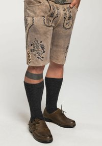 Braune Shorts mit aufwändiger blauer Stickerei, seitlichem Knopfdetail, kombiniert mit dunklen gestrickten Socken und braunen Schuhen.