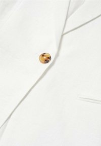 Gros plan d'un blazer blanc avec un seul bouton marron marbré et une petite poche sur le devant.