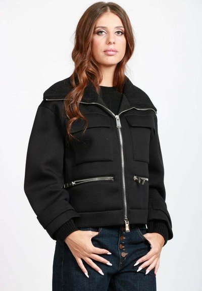 Giacca nera corta con zip metalliche, colletto testurizzato e tasche anteriori. Presenta un design aderente e polsini a costine.