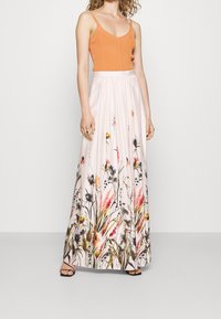 Maxiklänning med en orange figursydd linneöverdel och en flödande rosa kjol med blommönster i röda, gula och gröna nyanser.