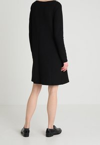 Czarna sukienka z długim rękawem o luźnym kroju, okrągłym dekolcie i długości do kolan. Gładka faktura i prosta, nieozdobiona forma.