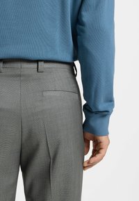 Grijze op maat gemaakte broek met een gestructureerde afwerking, gecombineerd met een blauw gebreid trui. De trui heeft een geribde boord en de broek heeft een achterzak.