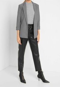 Blazer à carreaux gris avec un revers, porté sur un haut gris, associé à un pantalon en cuir noir taille haute et des bottines noires à talons pointus.