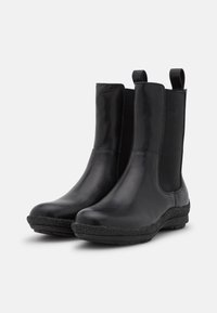 Botas negras hasta el tobillo con upper de cuero liso y paneles laterales elásticos. Presenta una suela de goma texturizada con un borde acolchado para mayor comodidad.