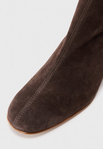 Stivale alla caviglia in suede marrone con punta affusolata, texture liscia e cuciture visibili. Presenta un tacco basso e rotondo e un design essenziale.