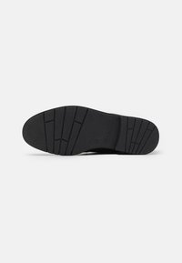 Suela de zapato de goma negra con una superficie texturizada, profundos surcos y un logotipo grabado en el talón. Bordes suaves para mayor durabilidad.
