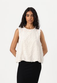Sleeveless cream top with textured, raised pattern, featuring a loose fit and round neckline. Paired with a black textured skirt.