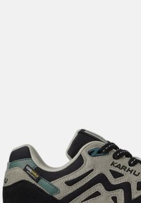 Svart och grå idrottssko med en texturerad mocka- och meshovandel, med gröna detaljer och en förstärkt häl, märkt med "KARHU."