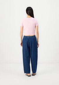 Camiseta corta rosa combinada con pantalones vaqueros oscuros de corte holgado. Los pantalones tienen una cinturilla elástica y un corte recto.