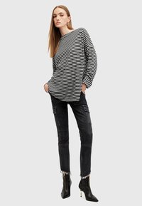 Camicia a maniche lunghe a righe in bianco e nero, abbinata a pantaloni cargo in denim nero con orli scrafatti e stivali neri con tacco alla caviglia.