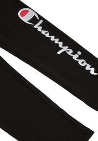 Pantaloni da tuta neri con una texture morbida, caratterizzati da un logo "Champion" in corsivo bianco e un accento rosso sulla "C."