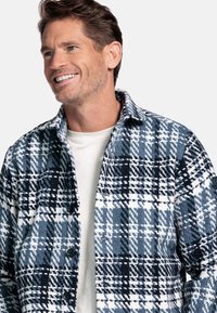 Geruit jasje in tinten blauw en wit; gemaakt van een gestoffeerde stof met een knoopsluiting en kraag; gelaagd over een licht shirt.