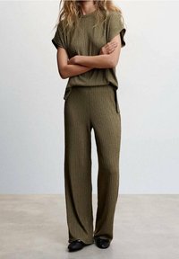 Set composto da top in maglia textured verde oliva e pantaloni larghi, con maniche corte e una vestibilità rilassata. Le scarpe nere slip-on completano l'outfit.