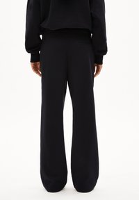 Schwarze weit geschnittene Sweatpants aus weichem Material, mit einem elastischen Bund und einer einzelnen Gesäßtasche auf der rechten Seite.