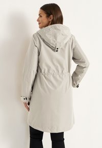 Helle graue wasserdichte Jacke mit Kapuze, tailliertem Schnitt und Druckknopfmanschetten. Glatte Textur mit minimalistischen Designelementen.