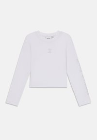 Balts garais piedurknes crop tops, kas izgatavots no mīksta kokvilnas, ar nelielu logotipu, kas izrotāts ar kristāliem krūtīs un dekoratīvu tekstu gar piedurknēm.