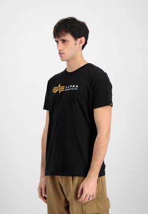Camiseta de algodón negra con un logo "ALPHA INDUSTRIES" en blanco y dorado. Corte ajustado con cuello redondo y mangas cortas.
