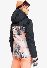 Black and pink floral ski jacket with a hood, featuring a glossy finish, elastic cuffs, and a vibrant orange beanie with goggles.