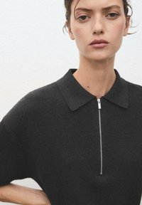 Dark gray polo-style top with a short zipper and a soft texture. Features a classic collar and loose-fitting sleeves.