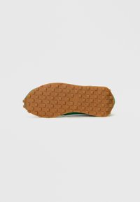 Sola do sapato com uma base de borracha castanha, apresentando saliências quadradas para tração, contornada por uma borda verde texturizada. Acabamento suave no material de borracha.