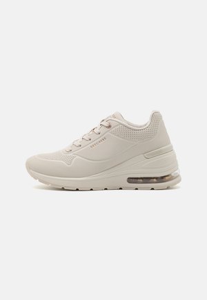 Beige atletiksko med en struktureret overflade, perforerede detaljer, snørebåndsdesign og en synlig luftpude i sålen.