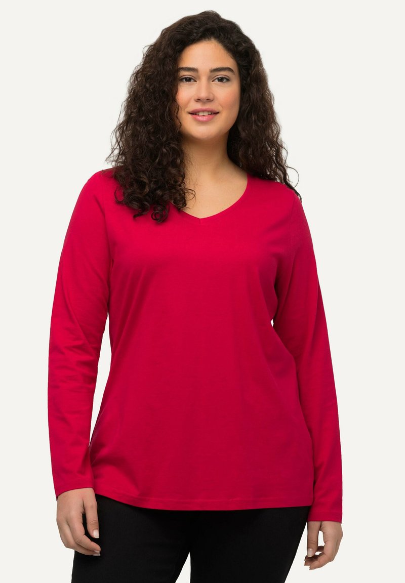 Dlouhý rukáv tričko s výstřihem do V v jasně červené barvě, vyrobeno z hladkého materiálu. Disponuje volným střihem se rovnoměrně zakončeným spodním lemem a měkkou texturou.