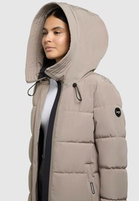 Helles beiges Daunenjacke mit großer Kapuze, schwarzen Akzenten, Reißverschluss und Zugbandschnürung. Besitzt ein Logo-Patch am Ärmel.