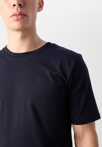 Tricou din bumbac de culoare bleu marin, cu mâneci scurte și decolteu rotund, având un logo mic brodat albastru pe piept.