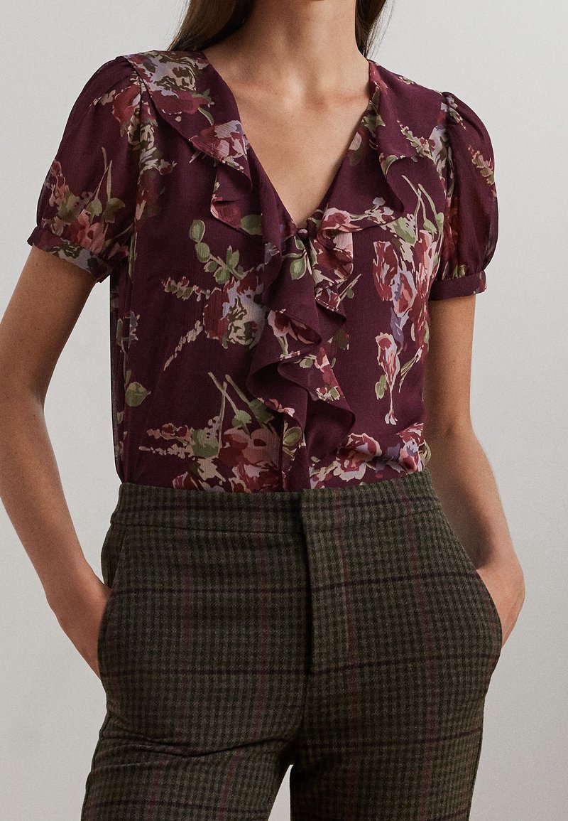 Blus med blommönster i djupt burgunderröd färg, med volangkrage och korta puffärmar, matchad med gröna rutiga byxor med hög midja.