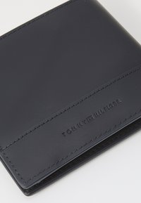 Mørkeblå skinnlommebok med en jevn tekstur, med sømte kanter og preget merkenavn langs bunnen. Kompakt, minimalistisk design.