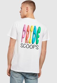 Valge puuvillane t-särk, millel on suured, värvilised "Pride" tähed roosa, oranži, rohelise, sinise ja kollase värviga, ning sõna "SCOOPS" all musta värviga.