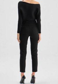 Pull noir côtelé à col bardot associé à un pantalon noir ajusté, avec deux poches arrière, et des chaussures noires à talons hauts.