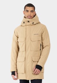 Beige geïsoleerde jas met een hoge kraag, meerdere voorzakken, verstelbare capuchon en zwarte manchetten. Materiaal lijkt glad en duurzaam.