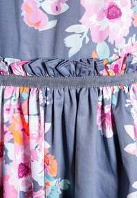 Close-up of blue fabric with pink, orange, and white floral pattern and a gathered, elastic waistband with ruffle detail.