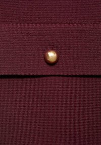 Mörkröd stickad tyg med ett texturerat mönster, med en framträdande bronsebutton som accentdetalj.