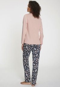 Hellrosa Langarmoberteil mit geradem Schnitt, kombiniert mit dunkelblauen Hosen, die ein florales Muster in Pfirsich und Weiß aufweisen. Glatte Stoffstruktur.