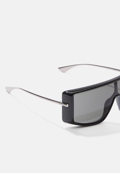 Melni taisnstūra saulesbrilles ar tumšiem lēcām un metālisku sudraba apdari, ar elegantiem, minimālistiskiem kātiem un spīdīgu tekstūru.