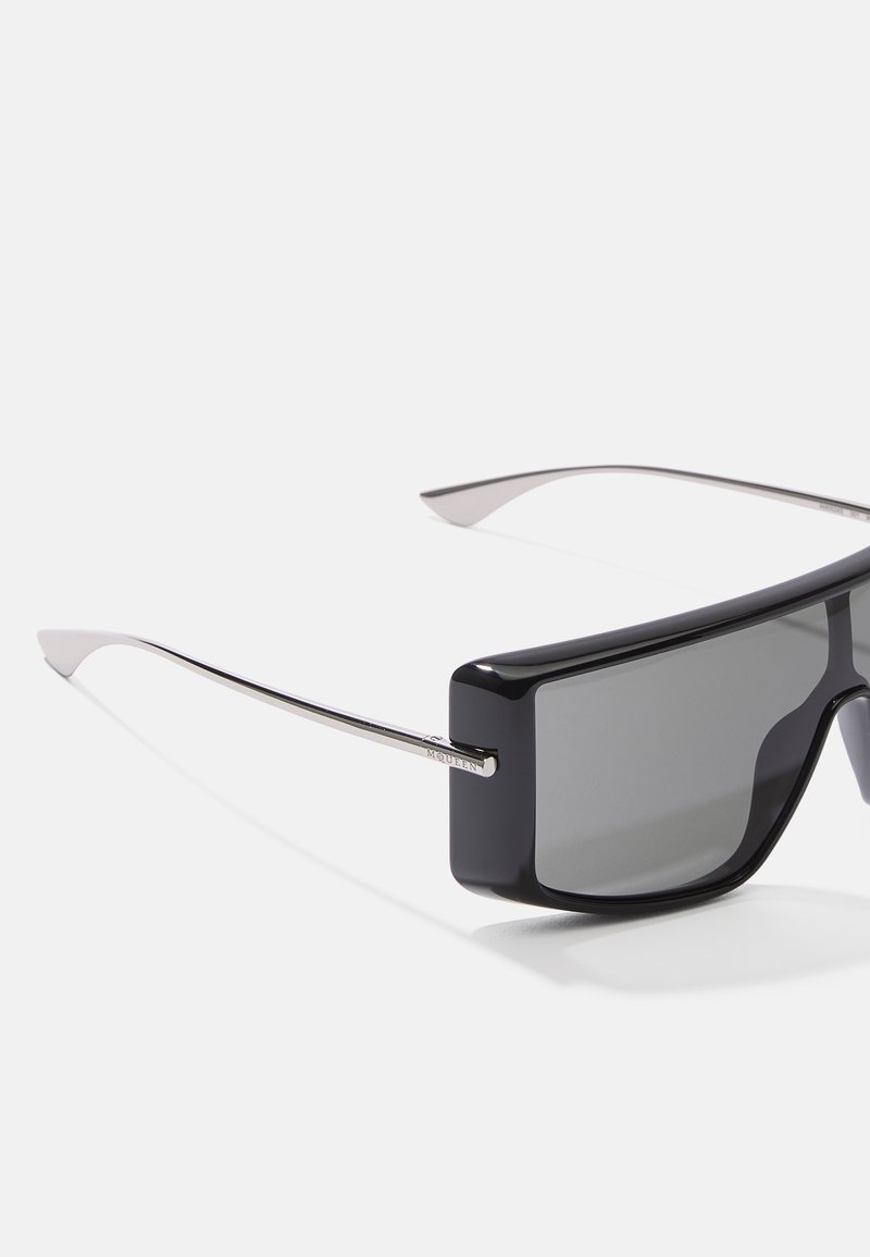 Schwarze rechteckige Sonnenbrille mit dunklen Gläsern und metallisch silbernen Akzenten, ausgestattet mit schlanken, minimalistischen Bügeln und einer glänzenden Oberfläche.
