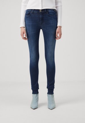 Jeans ajustados en denim azul oscuro con un ligero efecto desgastado, diseño de cinco bolsillos y una cintura de altura media, combinados con botas de tobillo azul claro.